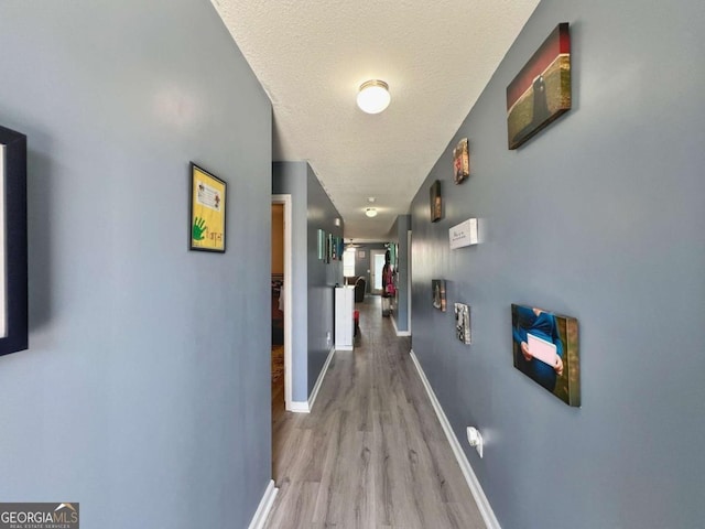 hall with light wood-type flooring, baseboards, and a textured ceiling