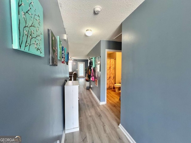 hall featuring wood finished floors, baseboards, and a textured ceiling