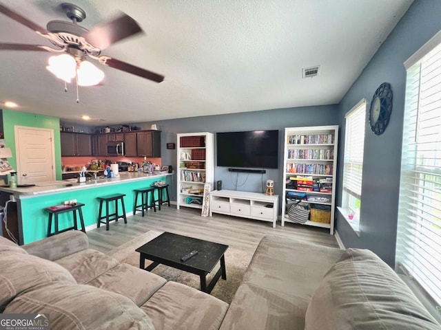 living room with a ceiling fan, light wood-style flooring, and a textured ceiling