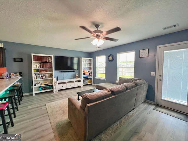 living room featuring a textured ceiling, light wood-style floors, a ceiling fan, and baseboards