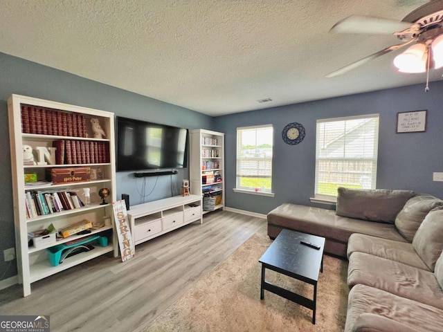 living area featuring wood finished floors, a textured ceiling, ceiling fan, and baseboards