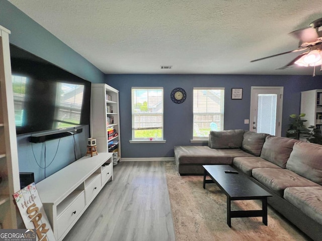 living area featuring ceiling fan, light wood-type flooring, a textured ceiling, and baseboards
