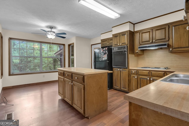 kitchen featuring black appliances, under cabinet range hood, wood finished floors, a textured ceiling, and a center island