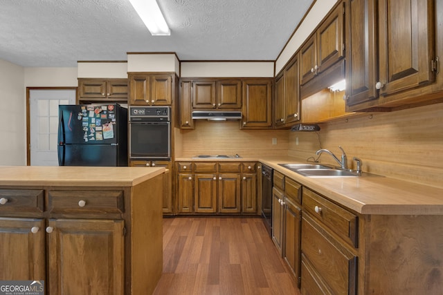 kitchen with black appliances, under cabinet range hood, dark wood finished floors, light countertops, and a textured ceiling