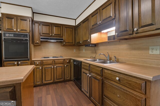 kitchen with black appliances, a sink, crown molding, dark wood-style flooring, and under cabinet range hood