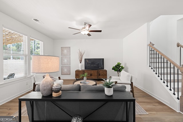 living area with ceiling fan, wood finished floors, baseboards, and stairway