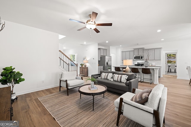 living room featuring ceiling fan, light wood-type flooring, recessed lighting, baseboards, and stairs