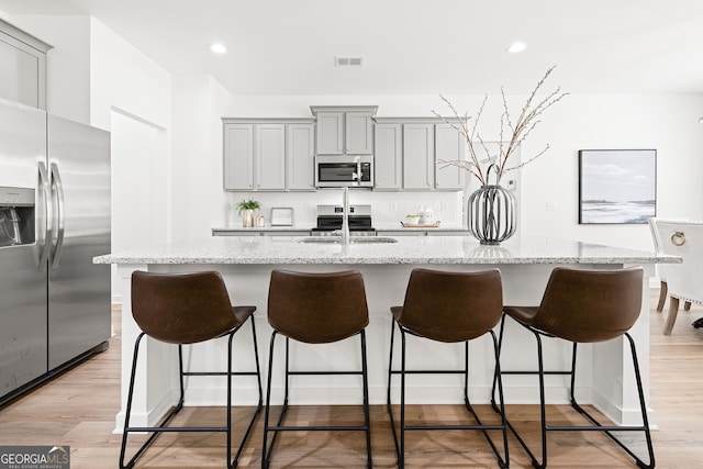 kitchen with appliances with stainless steel finishes, gray cabinets, a center island with sink, a breakfast bar, and recessed lighting