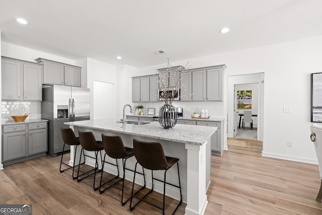 kitchen featuring stainless steel appliances, gray cabinetry, a sink, a breakfast bar, and recessed lighting