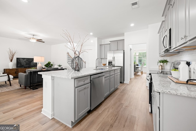 kitchen with stainless steel appliances, a sink, gray cabinetry, light wood finished floors, and light stone counters