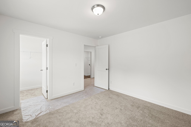 unfurnished bedroom with carpet flooring, a spacious closet, and baseboards