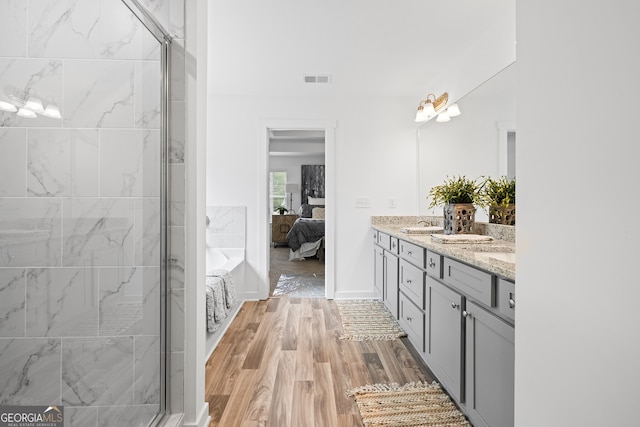 bathroom with a stall shower, wood finished floors, double vanity, and ensuite bathroom