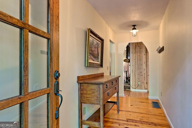 hall featuring arched walkways, light wood-type flooring, and baseboards