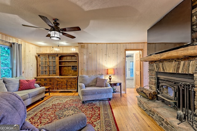 living area with light wood finished floors, a ceiling fan, wood walls, a wood stove, and a textured ceiling