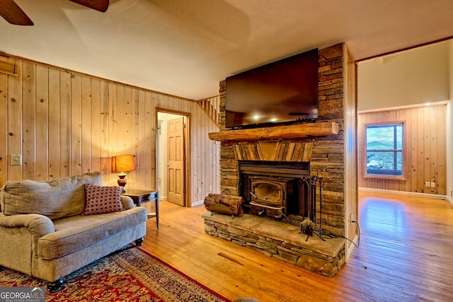 living area featuring wood-type flooring, wooden walls, ceiling fan, and baseboards