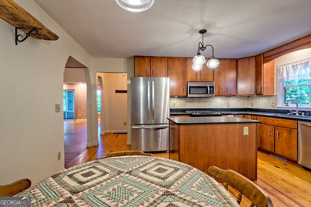 kitchen with appliances with stainless steel finishes, a sink, light wood-style floors, a center island, and dark countertops