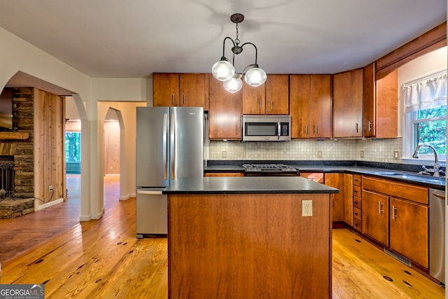 kitchen featuring appliances with stainless steel finishes, a sink, arched walkways, a center island, and light wood-style floors
