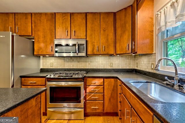 kitchen featuring appliances with stainless steel finishes, a sink, backsplash, light wood-style flooring, and brown cabinets