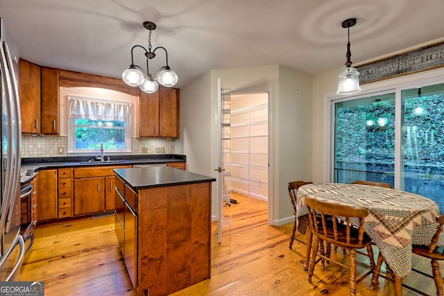 kitchen featuring a sink, a center island, light wood finished floors, brown cabinetry, and decorative backsplash