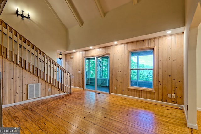 unfurnished living room featuring hardwood / wood-style flooring, stairway, high vaulted ceiling, beamed ceiling, and baseboards