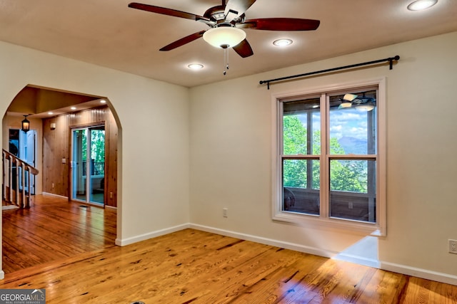 empty room featuring arched walkways, wood finished floors, baseboards, a ceiling fan, and recessed lighting