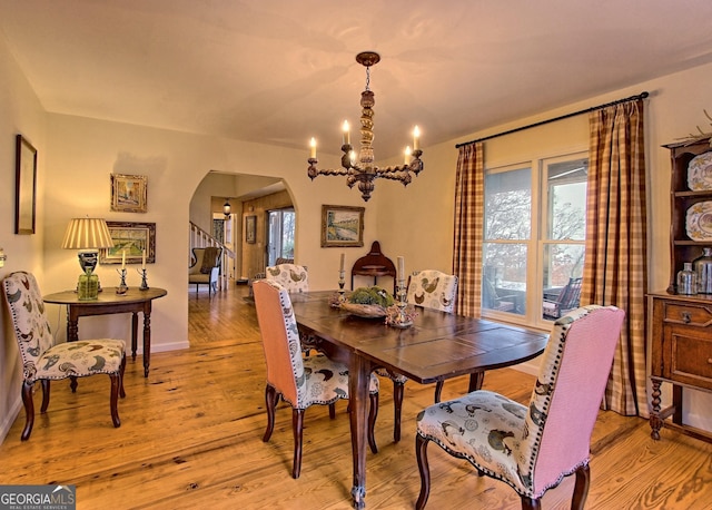 dining space featuring arched walkways, a chandelier, light wood finished floors, and baseboards