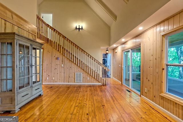 foyer entrance with wood-type flooring, wooden walls, stairs, and high vaulted ceiling