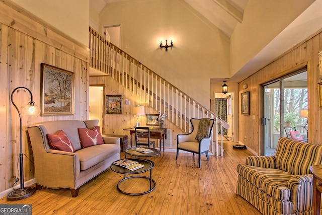 living room with stairway, high vaulted ceiling, hardwood / wood-style floors, wood walls, and baseboards