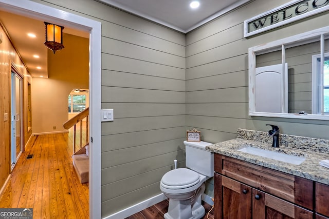 bathroom featuring hardwood / wood-style flooring, toilet, vanity, baseboards, and wooden walls