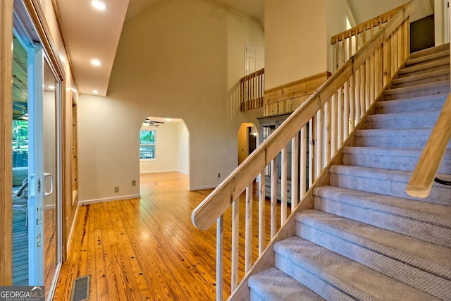stairs featuring arched walkways, hardwood / wood-style flooring, recessed lighting, baseboards, and a high ceiling