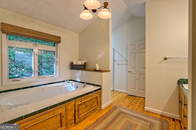 full bathroom featuring wood finished floors, a bath, vaulted ceiling, baseboards, and vanity