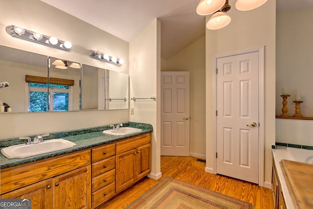 bathroom featuring wood finished floors, double vanity, and lofted ceiling