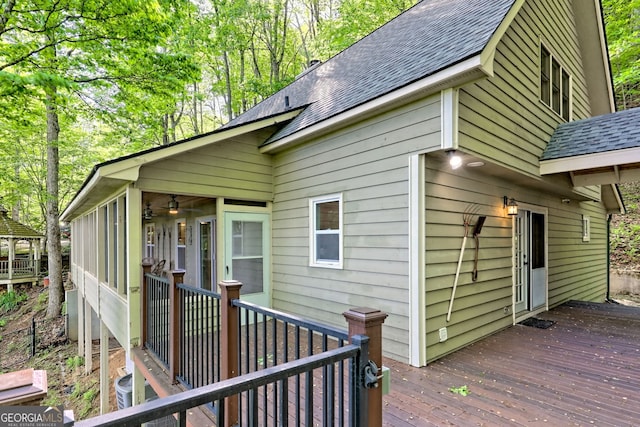view of property exterior featuring a wooden deck, a shingled roof, a sunroom, and central air condition unit