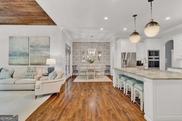 kitchen with appliances with stainless steel finishes, white cabinetry, light stone countertops, crown molding, and a kitchen bar