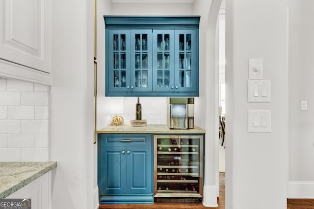 indoor dry bar with beverage cooler, wood finished floors, decorative backsplash, arched walkways, and baseboards