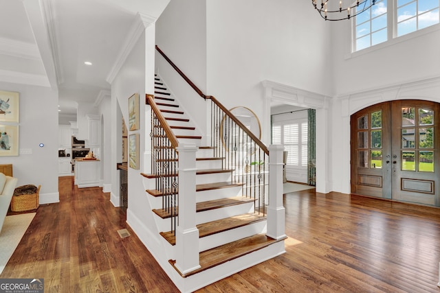 foyer with stairway, wood finished floors, ornamental molding, french doors, and a high ceiling