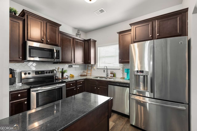 3406 Pennington Dr, Lithonia, GA 30038 - kitchen featuring stainless steel appliances, a sink, dark brown cabinetry, dark stone counters, and tasteful backsplash