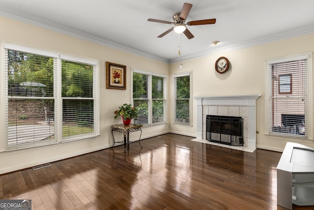 unfurnished living room with healthy amount of natural light, a tiled fireplace, crown molding, ceiling fan, and baseboards