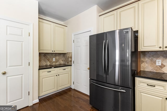 kitchen featuring cream cabinetry, freestanding refrigerator, dark countertops, dark wood finished floors, and tasteful backsplash