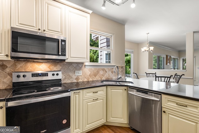 kitchen featuring stainless steel appliances, cream cabinetry, a sink, a chandelier, and backsplash