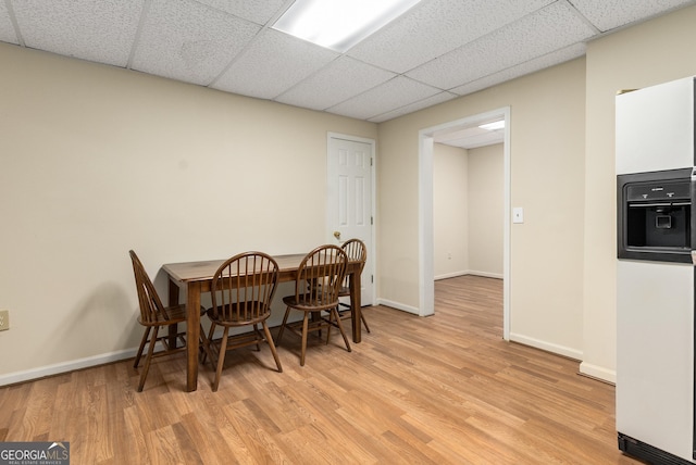 dining area with a drop ceiling, light wood-style floors, and baseboards