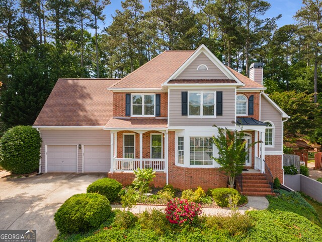 traditional-style house with a chimney, brick siding, an attached garage, and concrete driveway