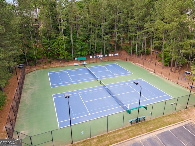 view of tennis court featuring fence, a forest view, and community basketball court