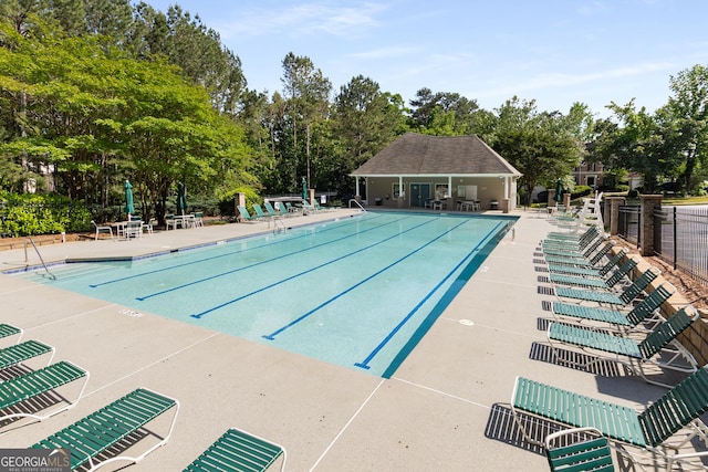 community pool with a patio, fence, and view of wooded area