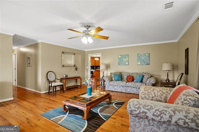 living area featuring wood finished floors, ceiling fan, ornamental molding, and baseboards