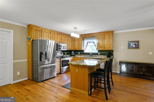 kitchen with appliances with stainless steel finishes, a sink, decorative backsplash, light wood finished floors, and a center island