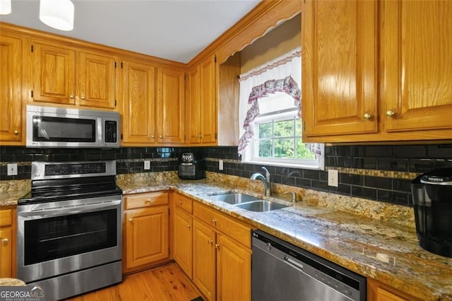 kitchen with stainless steel appliances, a sink, tasteful backsplash, and light stone countertops