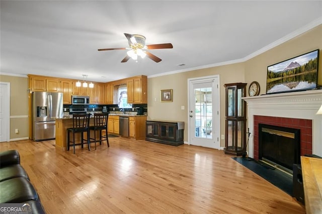 living room featuring a ceiling fan, light wood-style flooring, crown molding, baseboards, and a fireplace with flush hearth