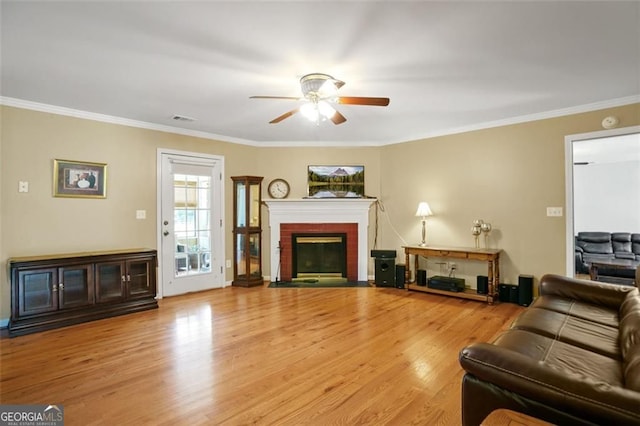 living room with a ceiling fan, wood finished floors, a fireplace, and ornamental molding