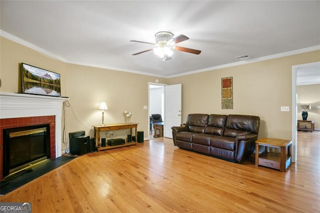 living room with a ceiling fan, wood finished floors, crown molding, and a fireplace